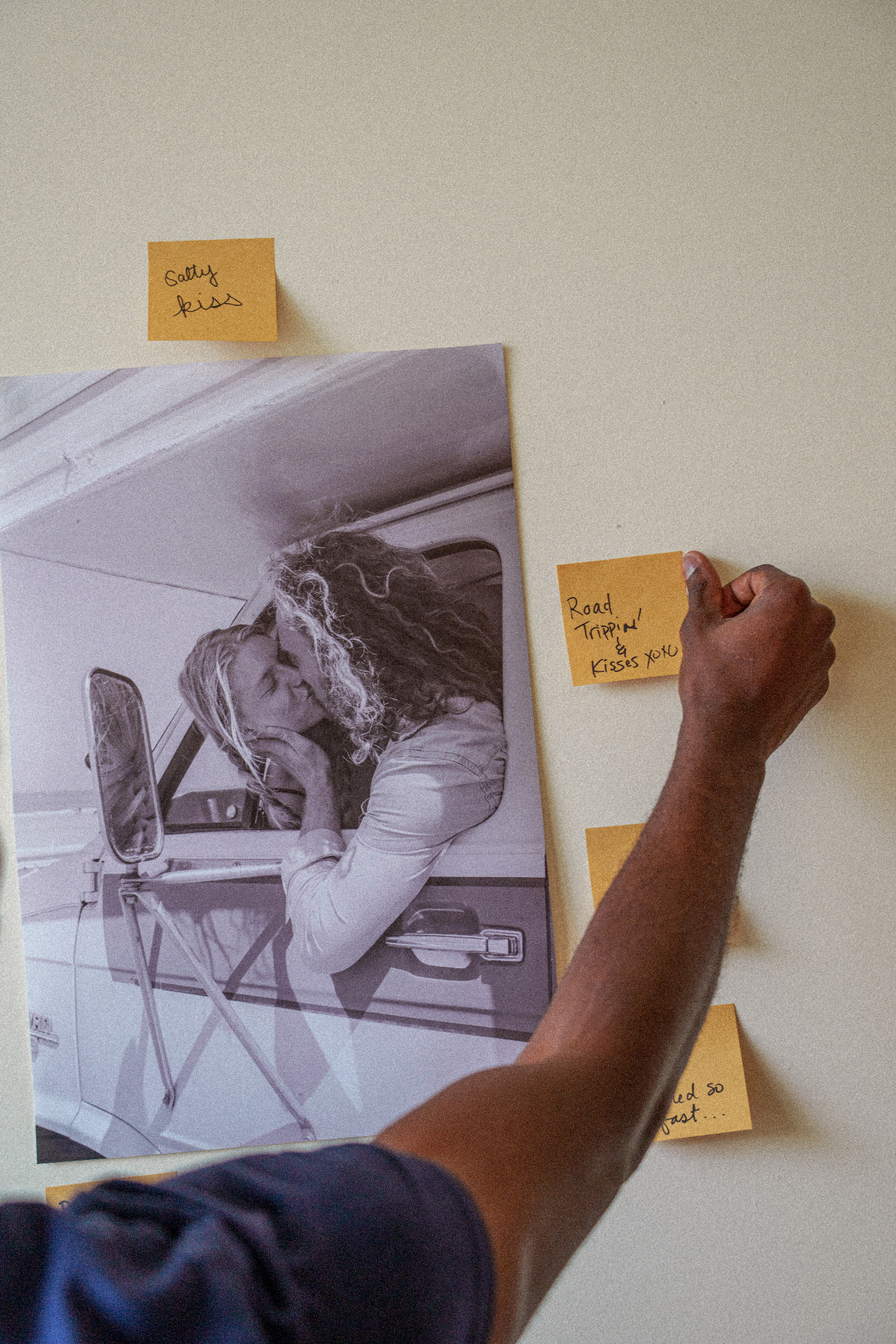 A hand pinning a note beside a black-and-white photograph on a studio wall